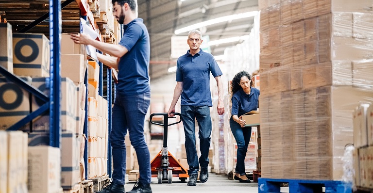 Three warehouse workers move packages onto pallets.