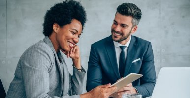 Black woman reviews her co-worker’s report on her tablet.